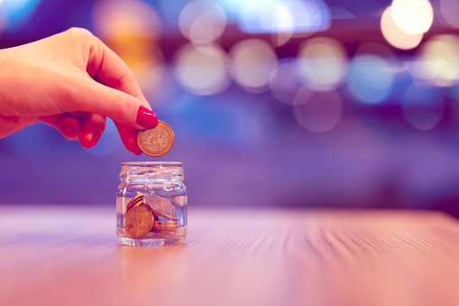 Close-up of a woman holding a drop of coins in a glass jar