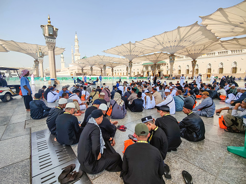 Medina, Saudi Arabia - March 07, 2023: Muslim pilgrims walk in the courtyard of Masjid al-Nabawi (Prophet's Mosque). As the final resting place of the Prophet Muhammad, it is considered the second holiest site in Islam by Muslims (the first being the Masjid al-Haram in Mecca).