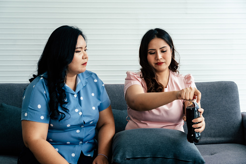 Overweight asian woman drinking soft drink in living room