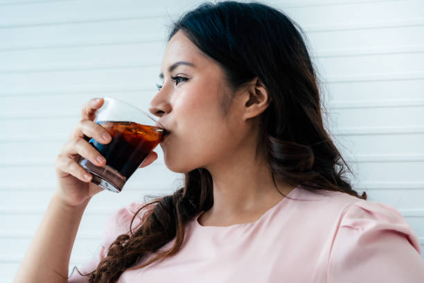 Overweight woman drinking soft drink Overweight asian woman drinking soft drink in living room coca cola stock pictures, royalty-free photos & images