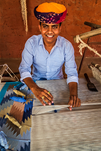 Indian man weaving durries. The durry (Rug) is weaved out of cotton or wool. The geometric designs are produced by tapestry technique which is a slow process using separate bobbins or butterflies for each colour across the width interlocking with the adjacent coloured yarn.  This old fashined form of weaving is very popular in Rajasthan, specially in Salawas village near Jodhpur.