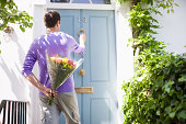 Man holding bouquet of flowers and knocking on door