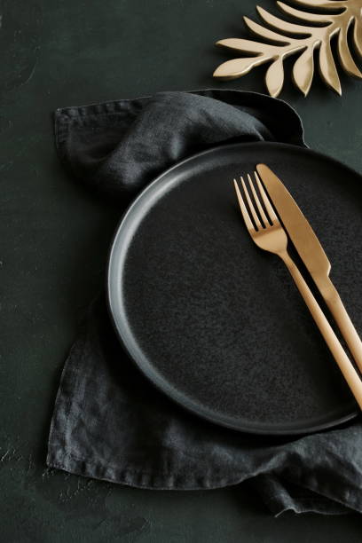 istock Empty black ceramic plate and cutlery on black background top view with copy space . Modern kitchen utensils.Space for text or menu .Business food brand template. 1717971890