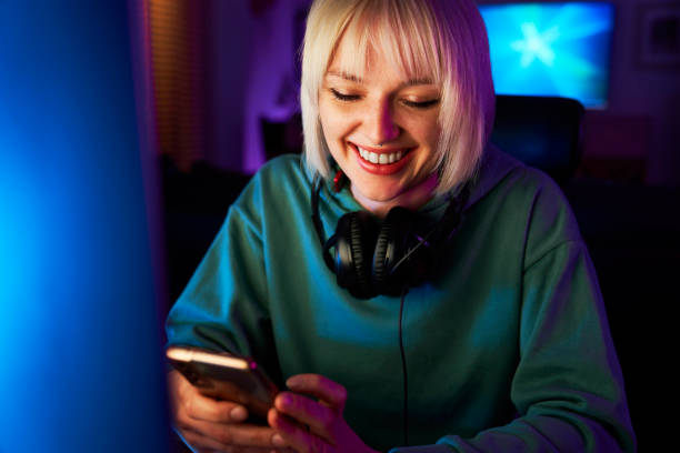 istock Cheerful young caucasian woman browsing mobile phone while a break during playing game at night on Desktop PC 1718030840