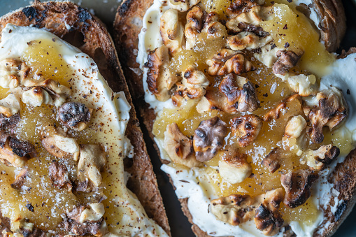 Two bread toast with cream cheese, roasted walnuts, honey, pepper and salt on plate, close up, top view