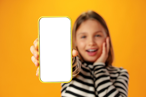 Teen girl showing smartphone screen with copy space over yellow background in studio
