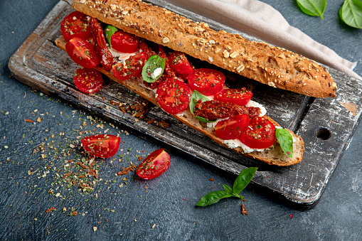 Fresh baguette with Caprese. Delicious sandwich with with tomatoes and mozzarella cheese with fresh basil leaves. Italian food conception.