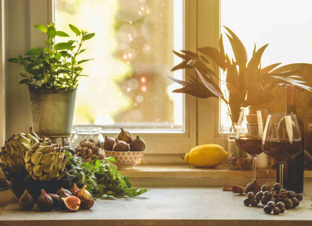 istock Kitchen table with figs, artichokes, red wine glasses, herbs and grapes at window background. 1718193538