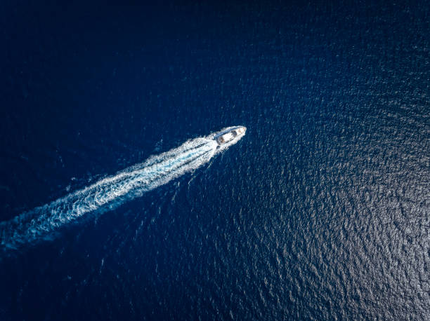 Aerial view of a yacht cruising over the ocean High aerial view of a luxury yacht traveling over the sparkling ocean sea wake stock pictures, royalty-free photos & images