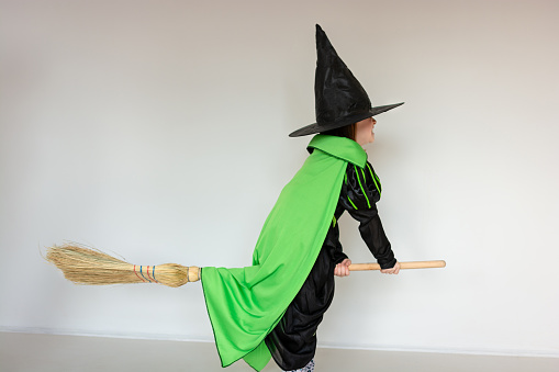 Full body shot of a female child dressed as a witch for Halloween as she rides a broomstick