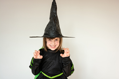Funny girl in witch costume for Halloween standing against white background and looking at camera