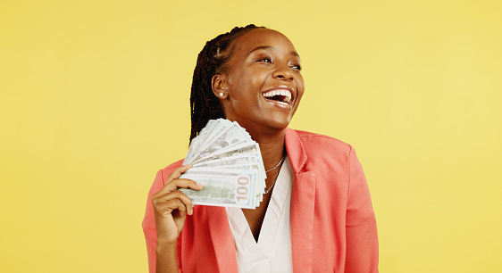 Money, fan and winner with a black woman in studio on a yellow background holding cash, finance or wealth. Financial, investment and trading with dollar bills in the hand of a female after winning