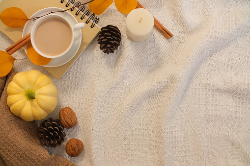 Vintage white fabric background and blank space for advertising. Pumpkins, coffee cups, notebooks and dried fruits are decorated in one corner of the frame. Autumn and Thanksgiving concept