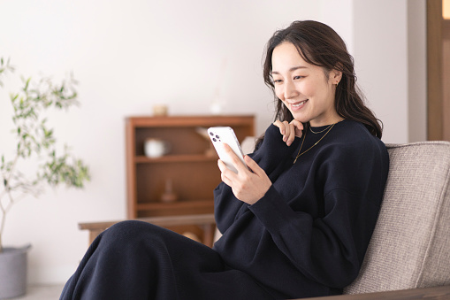 Asian woman looking at mobile phone in living room.She is sitting on the sofa.