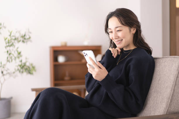 A Japanese woman life scene,she is looking at her phone. Asian woman looking at mobile phone in living room.She is sitting on the sofa. operating budget stock pictures, royalty-free photos & images