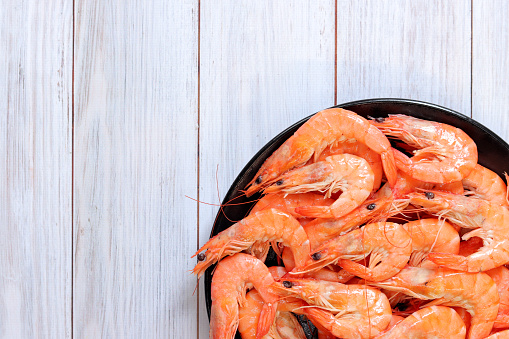 Boiled shrimp in a black plate on a light wooden background. Fresh shrimp, top view. Seafood. Healthy eating concept. Template for menu