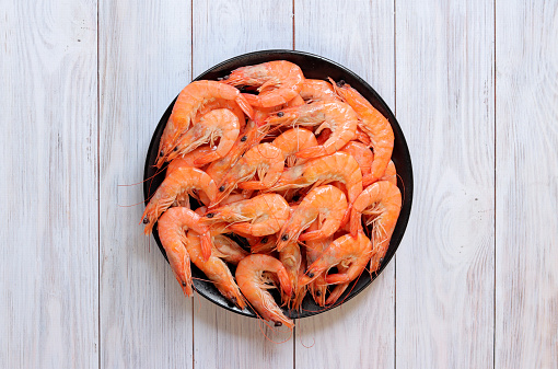 Boiled shrimp in a black plate on a light wooden background. Fresh shrimp, top view. Seafood. Healthy eating concept. Template for menu