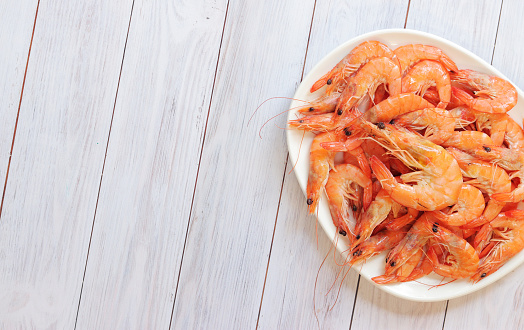 Boiled shrimp in a white plate on a light wooden background. Fresh shrimp, top view. Seafood. Healthy eating concept. Template for menu