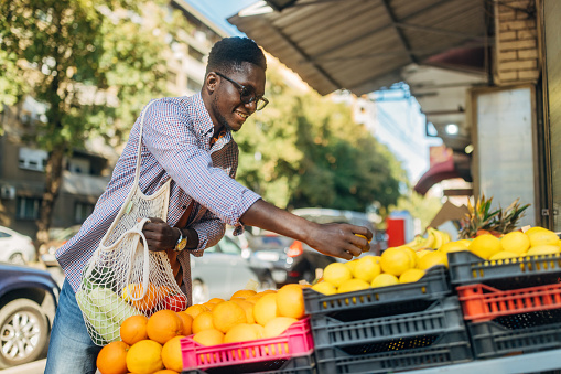 A healthy lifestyle man carries a reusable bag over his shoulder while choosing and buying fruit at the market