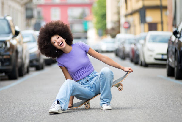 Happy young black woman sitting on skateboard
