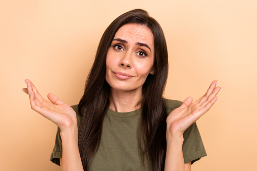 Portrait of clueless funny cute girl with long hairstyle wear t-shirt shrug shoulders say excuse me isolated on beige color background.