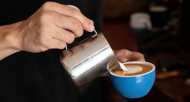 Photo of Barista pouring steamed milk to hot coffee to making latte art.