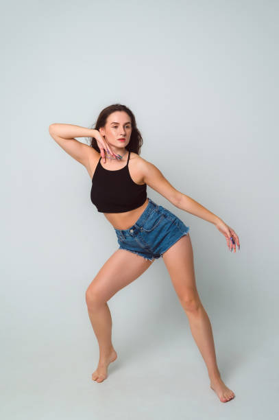 istock dancehall dancer posing on gray background in the studio, copy space. Full length portrait of beautiful young woman wearing black top and short denim shorts, barefoot 1718283526