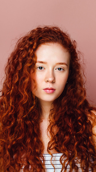 portrait of a cute curly girl on a pink background. Beautiful long red hair, no makeup