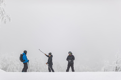 Group of male friends preparing for skiing and snowboarding in foggy winter day. One of them is showing something. Copy space.