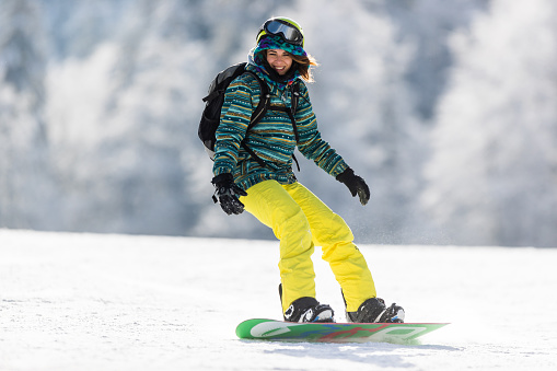 Young happy woman having fun while snowboarding in winter day. Copy space.