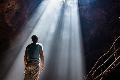 Low angle view of a man from the back standing in a cave and looking at the sunbeam. Copy space.