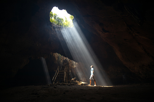 Full length of a man standing in the cave and looking at sunlight entering.