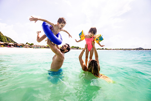 Happy parents having fun with their small kids during summer day in the sea. Copy space.