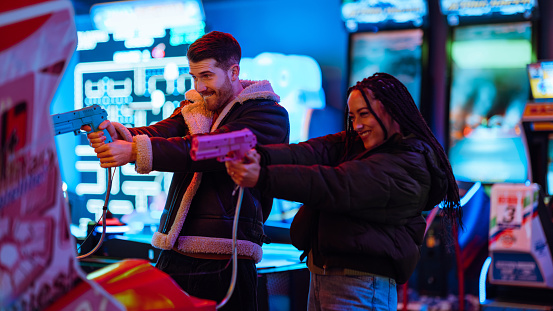 A mid adult couple spending the day at an amusement arcade together during a day in winter in Whitby, North East England. They are holding plastic toy guns and playing on a shooting game at the arcade while they focus on the target on the screen.

Videos are also available for this scenario.