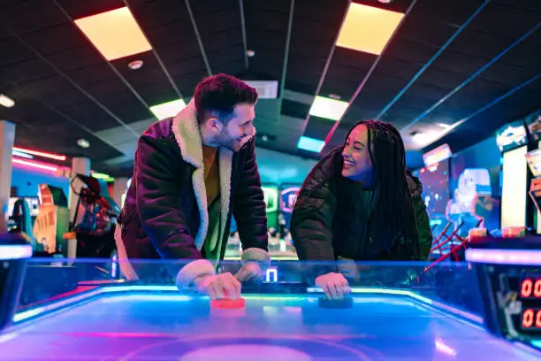 A mid adult couple on a date, spending the day at an amusement arcade together during a day in winter in Whitby, North East England. They are playing air hockey together against an unrecognisable opponent and the main focus is them holding onto handheld discs and looking excited while also looking at each other.

Videos are also available for this scenario.