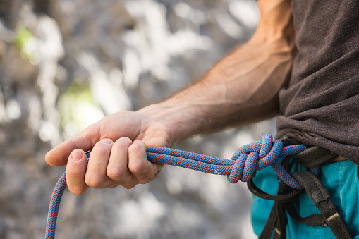 Close-up of rock climber arm and knot rope. Outdoor climbing concept.