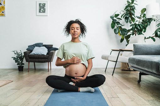 Young black pregnant woman doing relaxing exercises at home. Stretching yoga exercises are very beneficial for pregnancy
