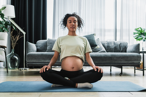 Young black pregnant woman doing relaxing exercises at home. Stretching yoga exercises are very beneficial for pregnancy