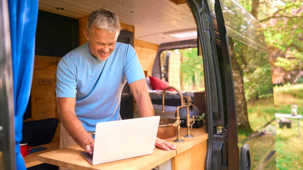istock Senior Man On Camping Trip In Countryside Working Inside RV Using Laptop 1718357000