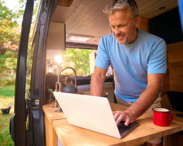 istock Senior Man On Camping Trip In Countryside Working Inside RV Using Laptop 1718359700
