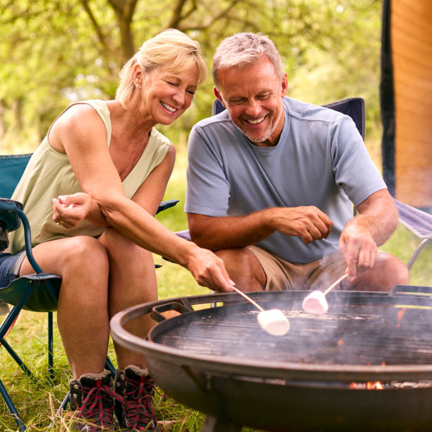 istock Senior Couple Camping In Countryside With RV Toasting Marshmallows Outdoors On Fire 1718371094