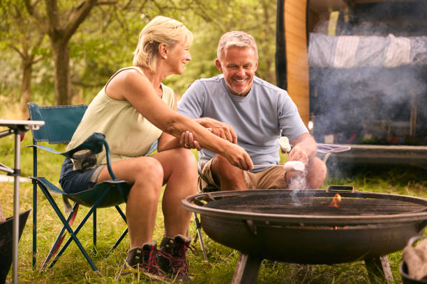 istock Senior Couple Camping In Countryside With RV Toasting Marshmallows Outdoors On Fire 1718378294