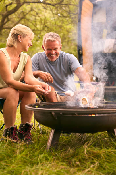 istock Senior Couple Camping In Countryside With RV Toasting Marshmallows Outdoors On Fire 1718381019