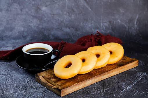Plain Donuts with cup of black coffee served on wooden board isolated on napkin side view of baked food breakfast on table