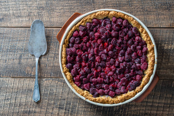 Raspberry pie in a ceramic dish on wooden background, close up, top view