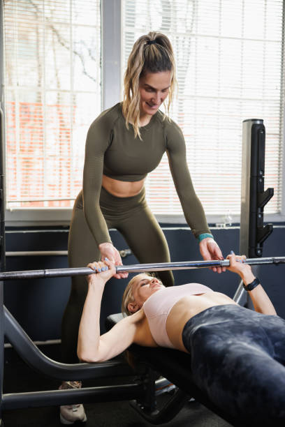 istock Woman doing lying barbell bench press, assisted by female gym instructor 1718418029