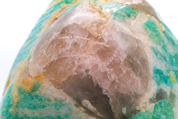 A tumbled chunk of light green and blue amazonite crystal with a clear quartz matrix focused and isolated on a white surface background