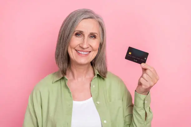 Photo of pensioner woman wearing khaki shirt holding black premium terms mastercard plastic advertise isolated on pink color background.