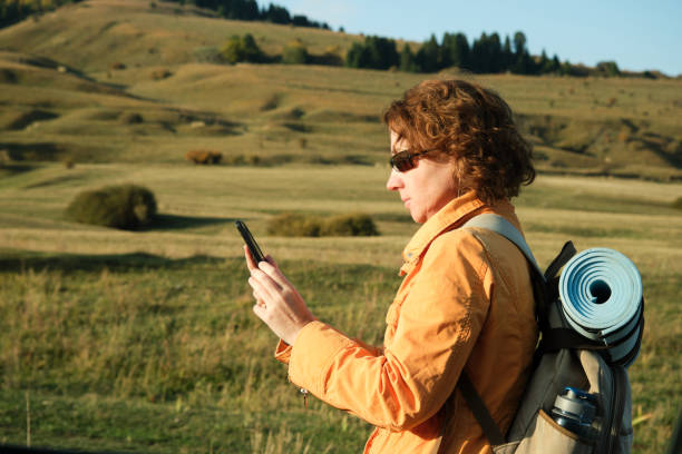 turista femenina camina por la carretera de la montaña y usa el teléfono - travel destinations mountain hiking profile fotografías e imágenes de stock