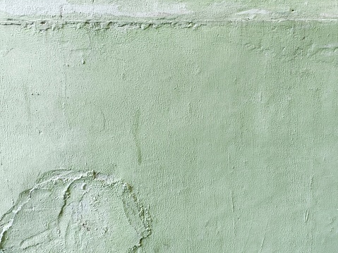 Detail of weathered green wall with faded paint and rough patches of plaster